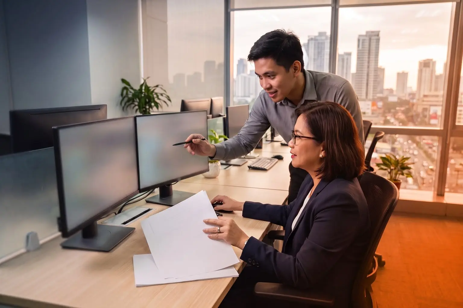 Two Filipino enterprise-systems professionals reviewing a workstation in a Metro Manila office under navy and orange lighting